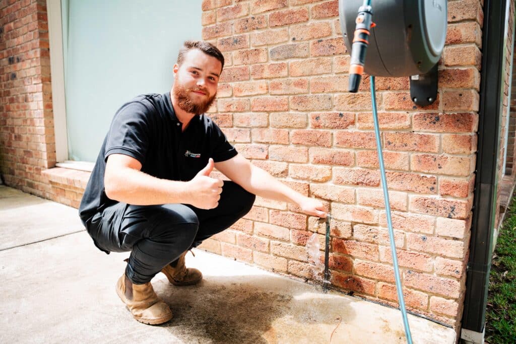 Plumber kneeling next to outdoor tap and exposed pipes