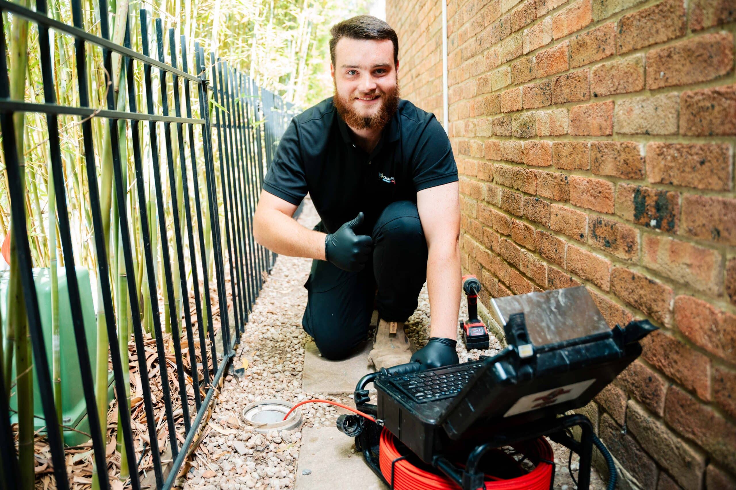 Champion Plumbing and Drains technician giving a thumbs up beside a CCTV drain camera during a drain inspection at a residential property