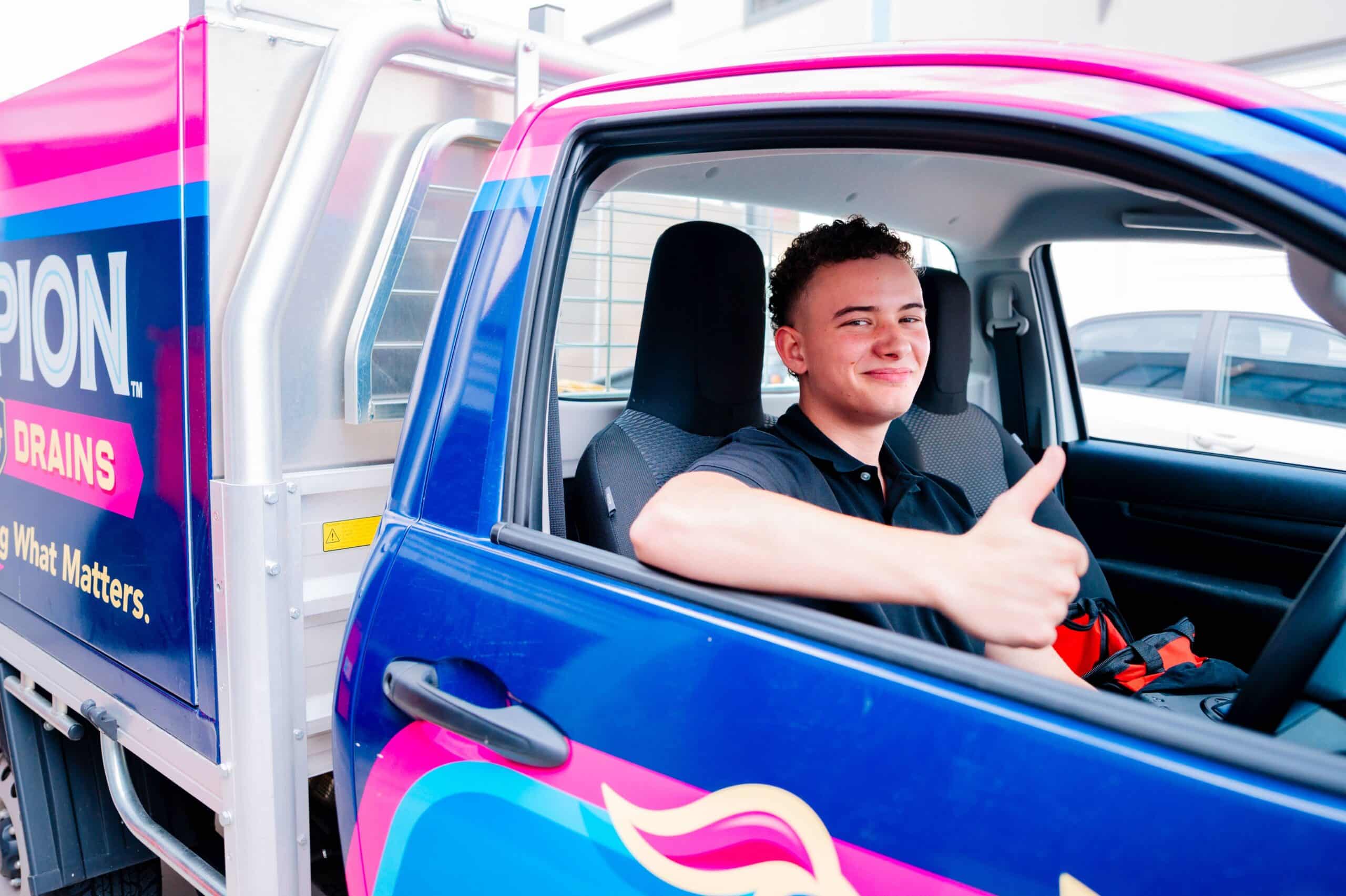 Champion Plumbing and Drains apprentice giving a thumbs up from inside a branded service truck, ready to head out on a job