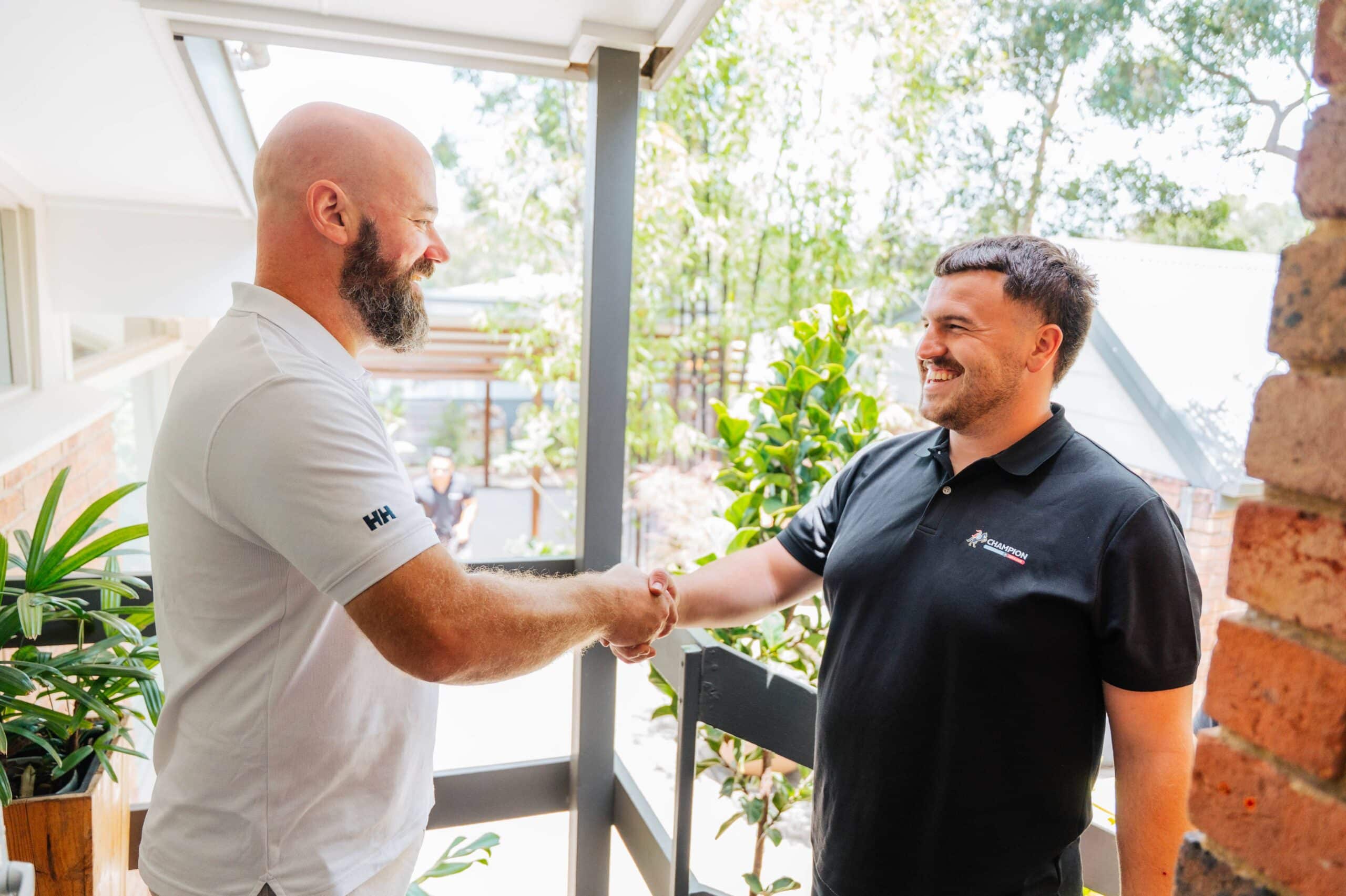 Champion Plumbing and Drains technician greeting a customer with a handshake at the front door of a residential home