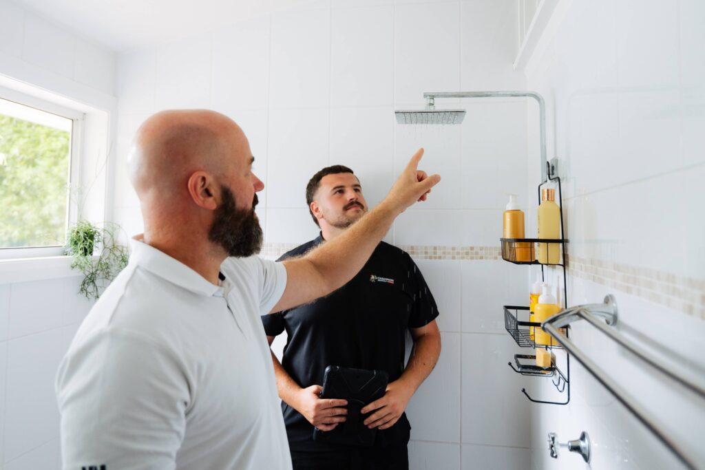 Champion Plumbing and Drains technician pointing out a shower fitting issue to a homeowner during a bathroom inspection