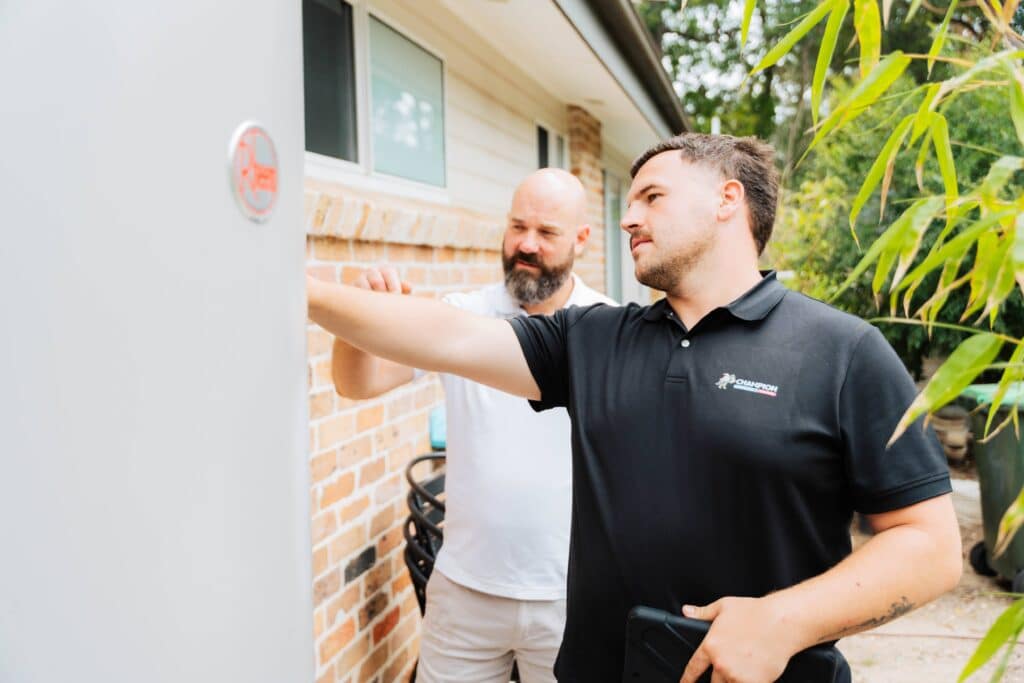 Champion Plumbing and Drains technician inspecting an external hot water unit with a homeowner at a residential property
