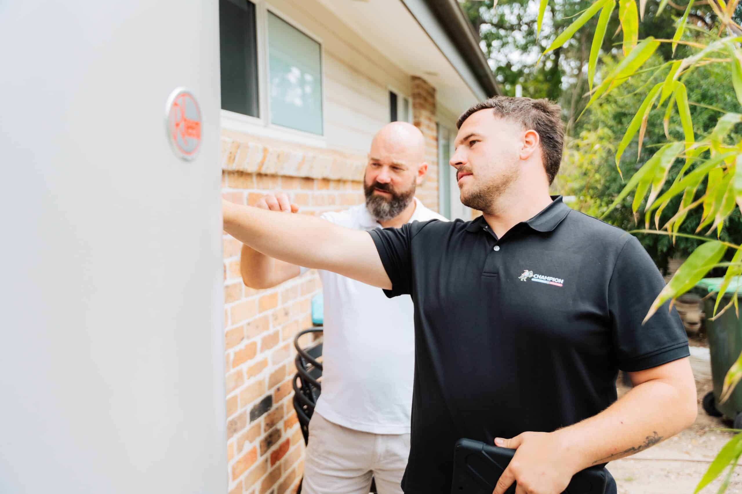 Champion Plumbing and Drains technician inspecting an external hot water unit with a homeowner at a residential property