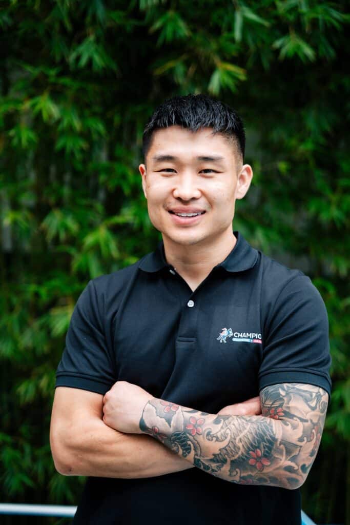 Champion Plumbing and Drains founder smiling with arms crossed in a portrait set against a bamboo backdrop
