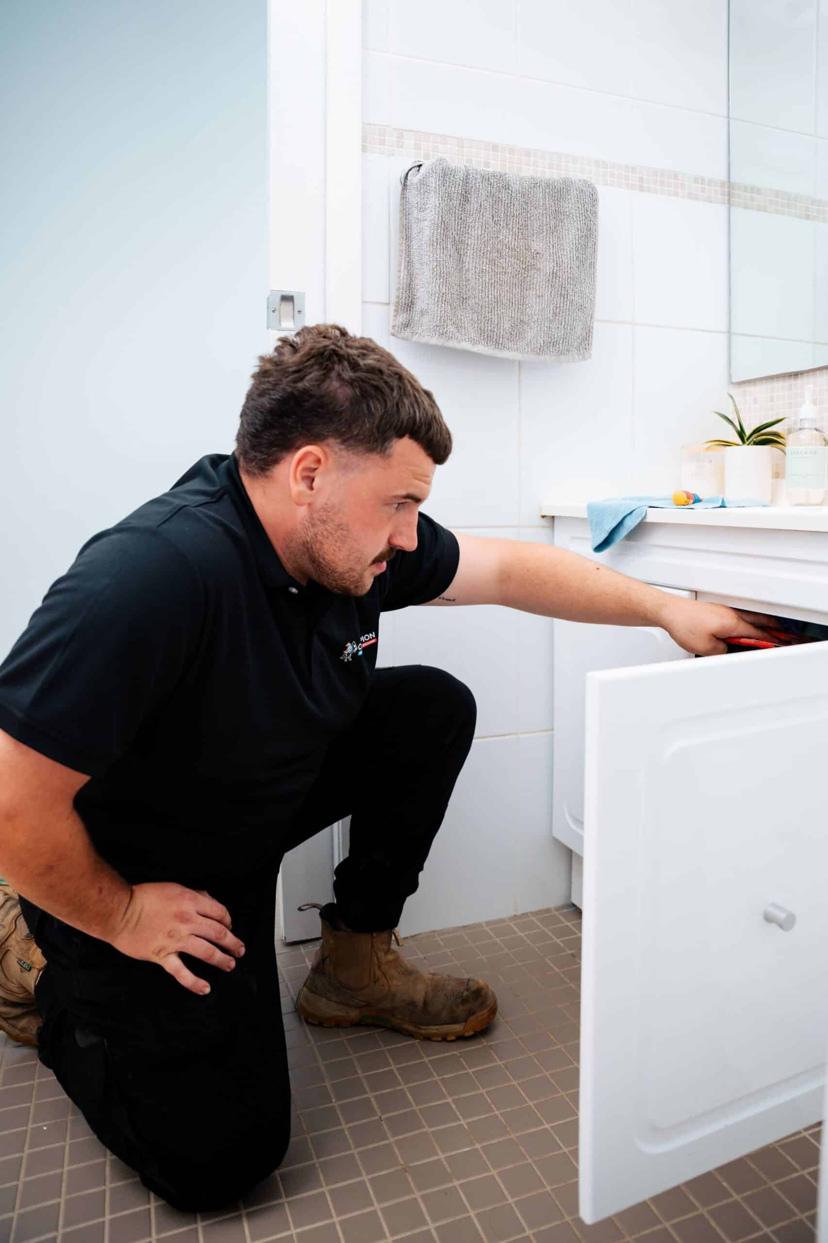 Champion Plumbing and Drains technician crouching to inspect the underside of a bathroom vanity cabinet