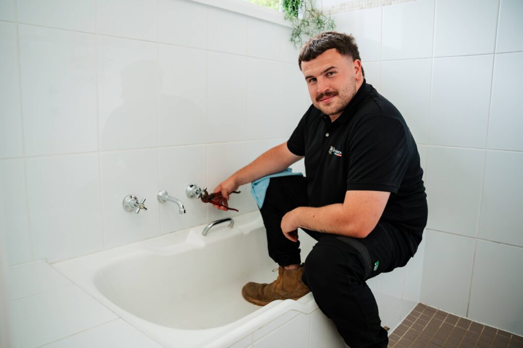 Champion Plumbing and Drains technician repairing a bathtub tap fitting using a wrench in a residential bathroom