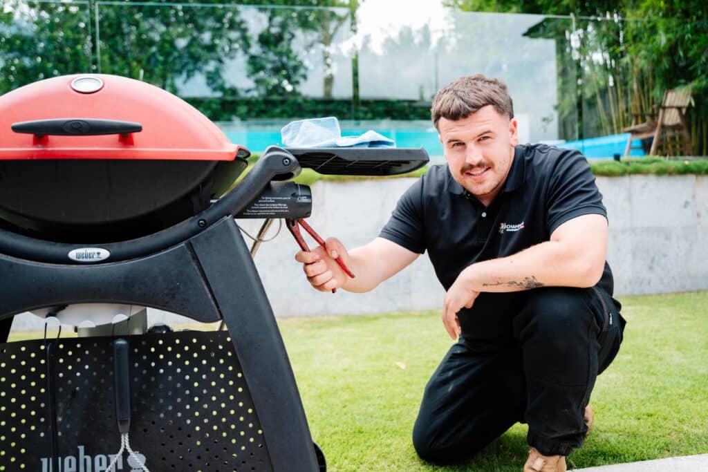 Champion Plumbing and Drains technician connecting a gas fitting on an outdoor Weber barbecue at a residential property