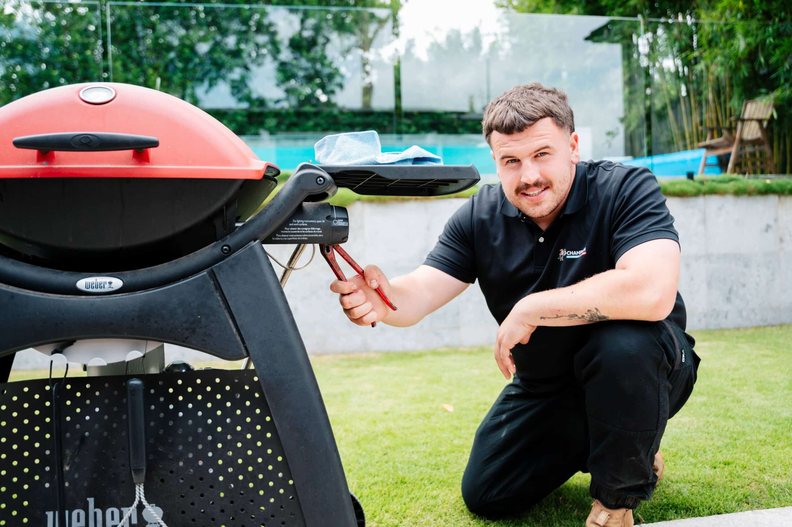 Champion Plumbing and Drains technician connecting a gas fitting on an outdoor Weber barbecue at a residential property