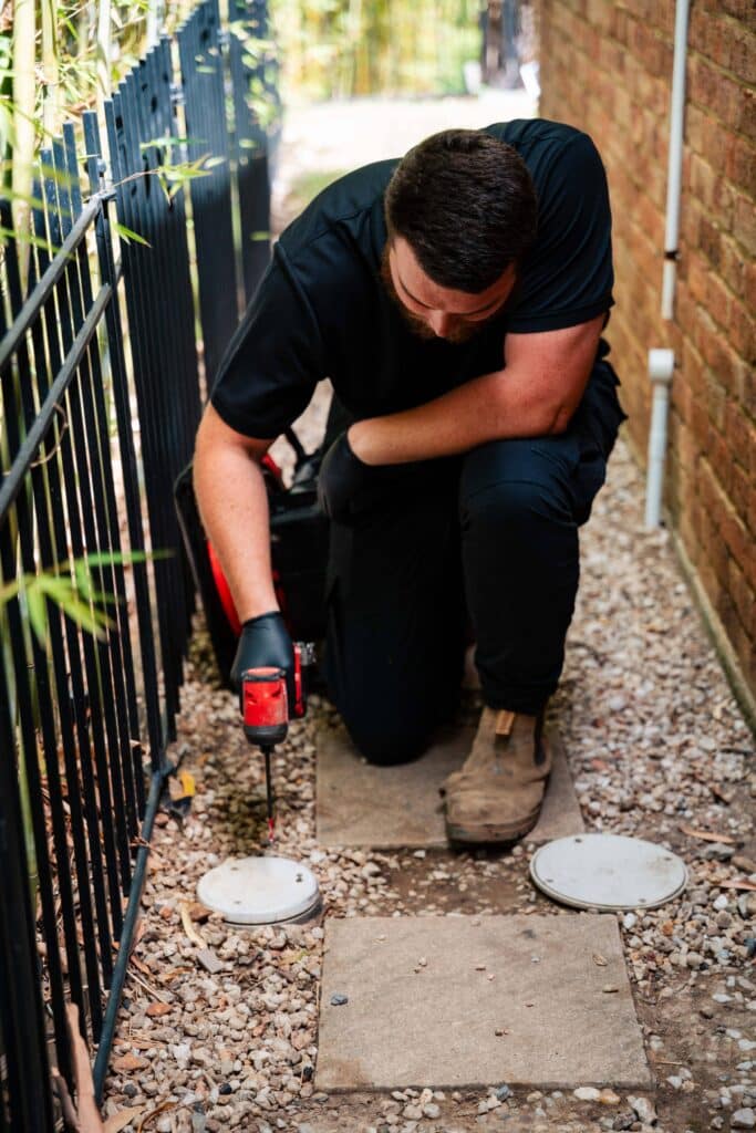 Champion Plumbing and Drains technician using a drain machine to clear a blocked drain in a narrow side passage at a residential property