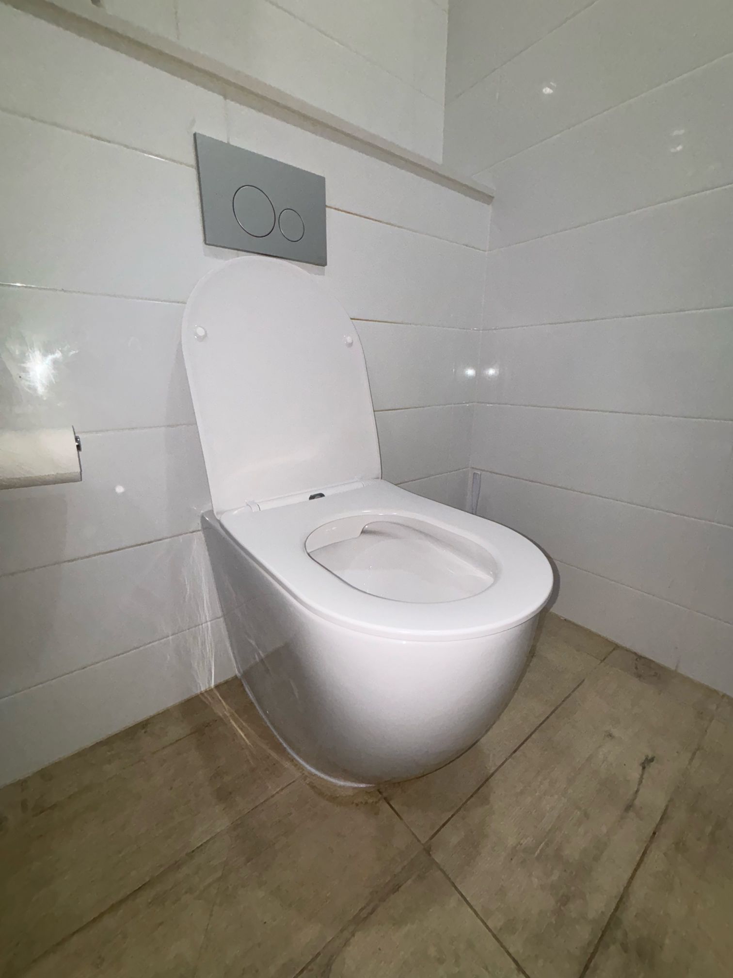 Newly installed white wall-faced toilet with a concealed in-wall cistern and chrome dual flush button