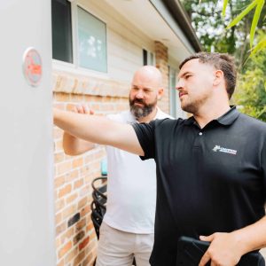 Champion Plumbing and Drains technician inspecting an external hot water unit with a homeowner at a residential property